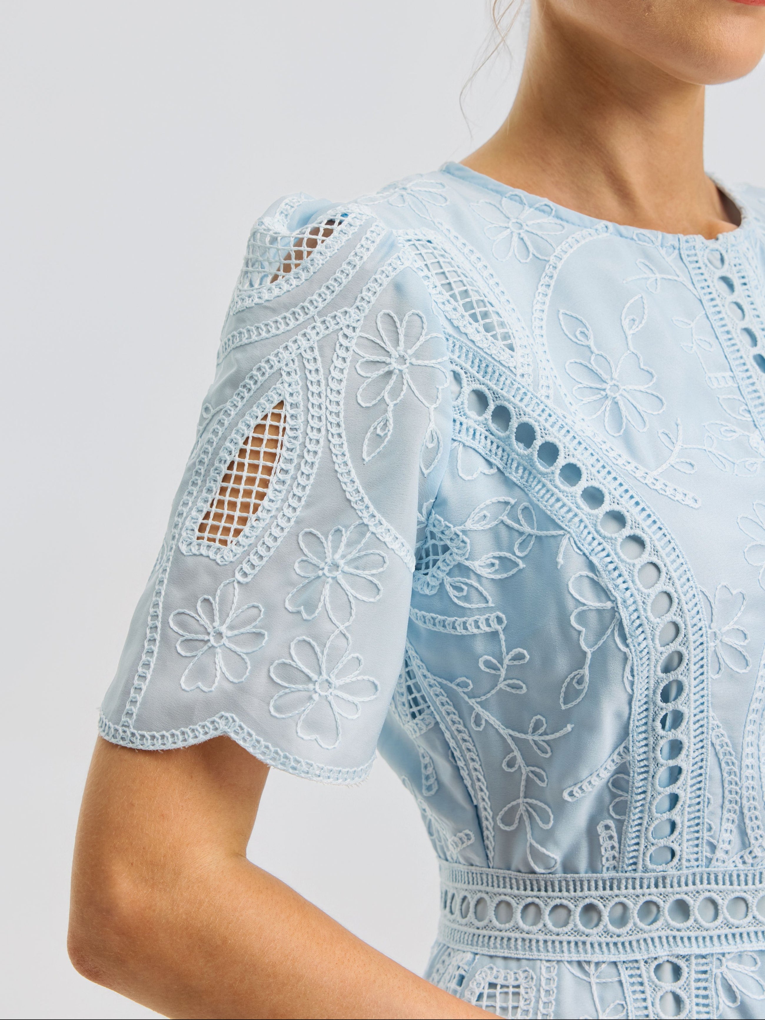 Close-up of a woman wearing the Floral Cutwork Embroidered Dress by Social Queen, crafted in a light blue silk-blend and adorned with floral embroidery, featuring intricate eyelet details and cutouts on the short sleeves.