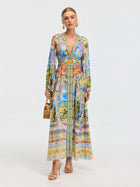 A woman wears the Social Queen Garden Print Silk Maxi Dress, styled with gold sandals, hoop earrings, and a bamboo handbag, set against a plain light background.
