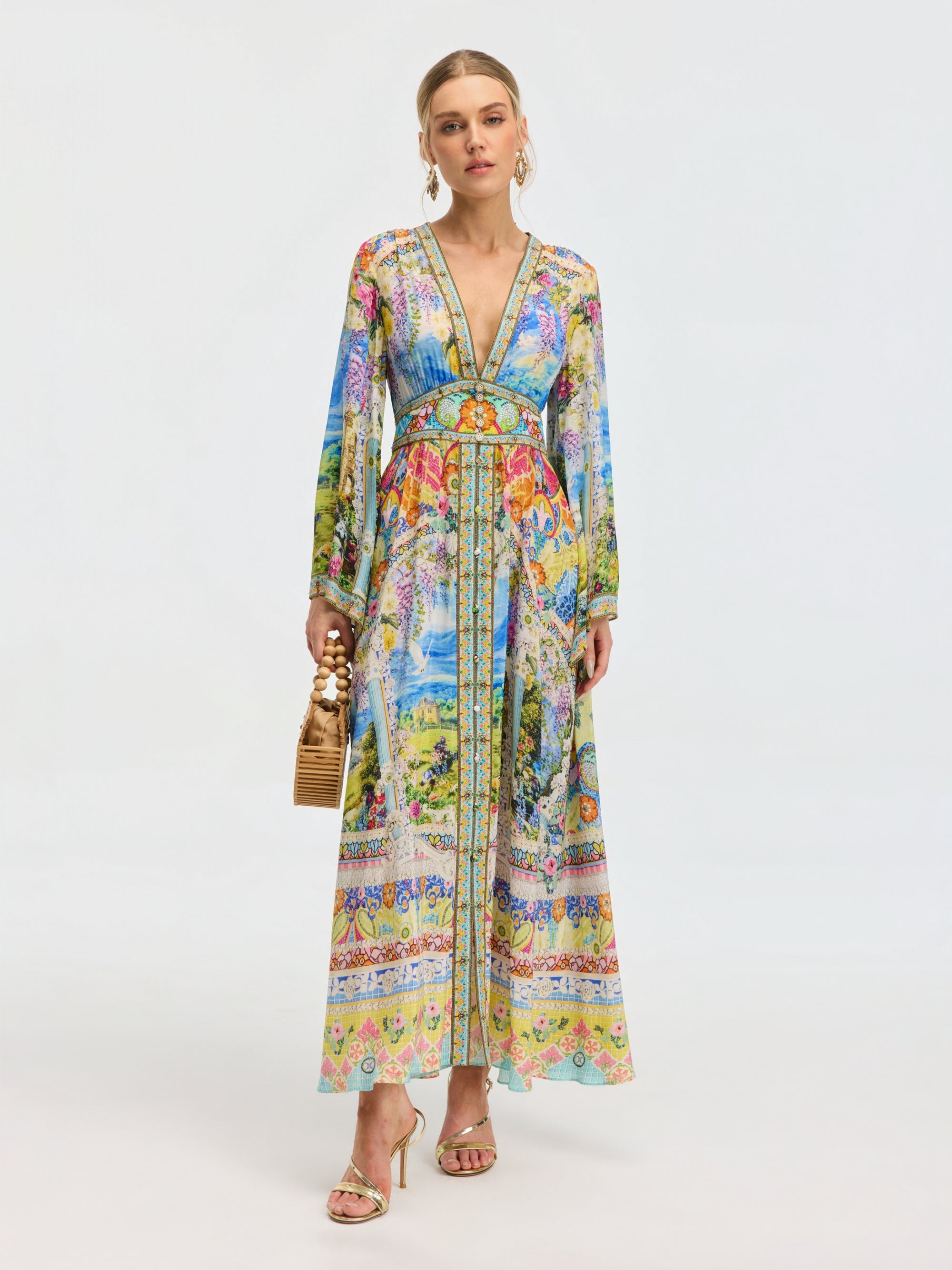 A woman wears the Social Queen Garden Print Silk Maxi Dress, styled with gold sandals, hoop earrings, and a bamboo handbag, set against a plain light background.