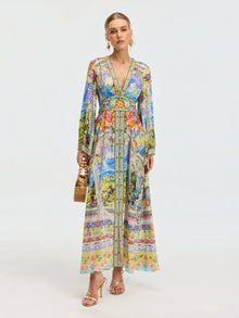 A woman wears the Social Queen Garden Print Silk Maxi Dress, styled with gold sandals, hoop earrings, and a bamboo handbag, set against a plain light background.