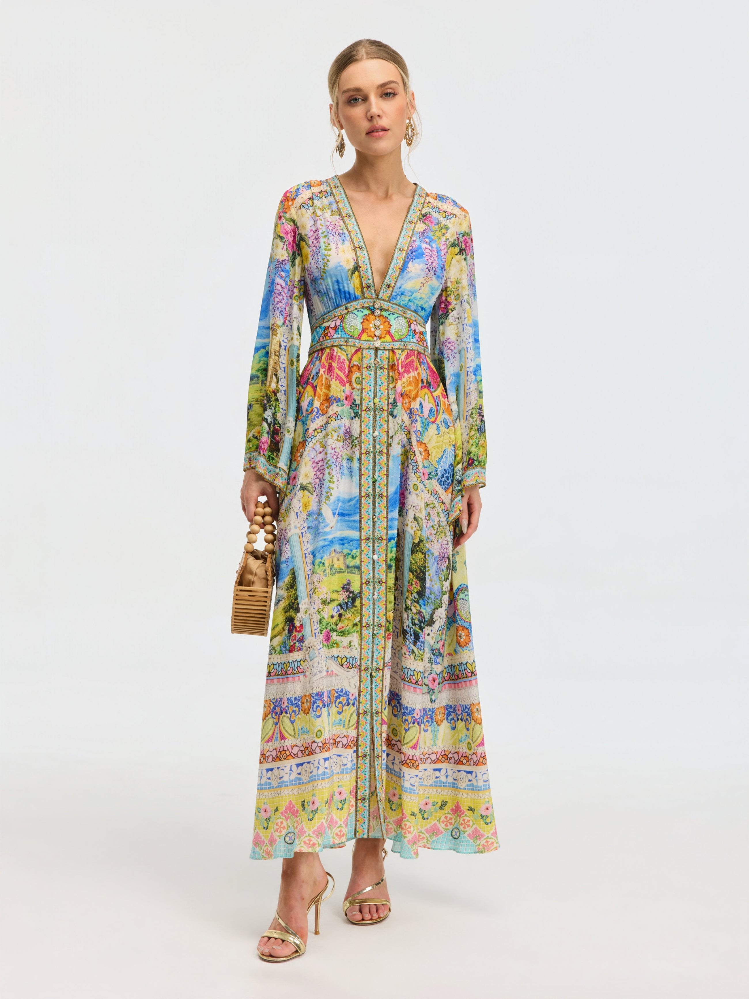 A woman wears the Social Queen Garden Print Silk Maxi Dress, styled with gold sandals, hoop earrings, and a bamboo handbag, set against a plain light background.