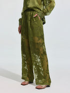 Model wears Social Queen’s Botanical Burnout Satin Wide-Leg Pants in olive green with a matching top and metallic strappy sandals, standing against a plain light background.