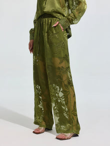 Model wears Social Queen’s Botanical Burnout Satin Wide-Leg Pants in olive green with a matching top and metallic strappy sandals, standing against a plain light background.