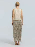 A woman stands facing away, wearing the Social Queen Floral Beaded Mesh Sleeveless Top paired with a long skirt featuring silver fringe, set against a plain light background.