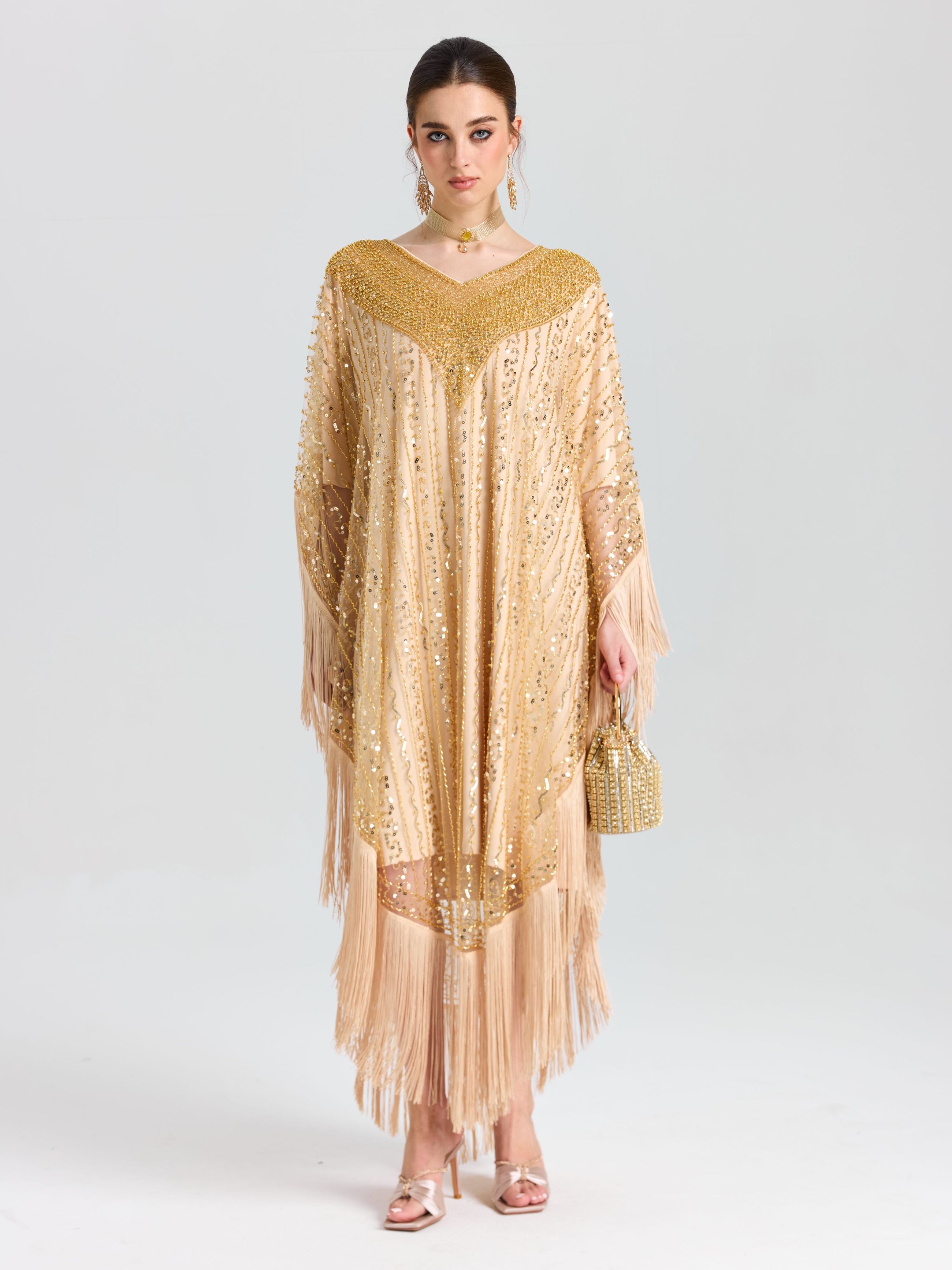 A woman faces forward in the Social Queen Beaded Fringe Cape Dress, styled with matching earrings and a small beaded handbag. She wears light makeup and has her hair pulled back.
