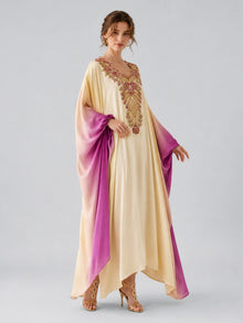 A woman wears the Social Queen Ombré Beaded Embroidered Cape Dress, featuring cream and purple tones with gold and pink beadwork, standing against a plain gray background.