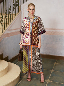 A woman stands on a tiled floor near stairs, wearing the Social Queen Patchwork Print Cotton Shirt Dress (belt included), paired with sandals and holding a brown handbag, with light-colored walls in the background.