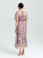 A woman faces away in the Social Queen Floral Beaded A-Line Dress, featuring lavender floral embroidery and sheer short sleeves, paired with nude heels against a plain light background.