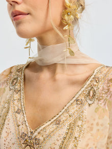 A woman wearing a sheer beige choker, Social Queen Floral Pearl Drop Earrings with a gold-tone finish, and a heavily beaded floral dress with intricate embroidery.