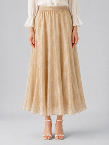 A person wearing the Social Queen Jacquard Chiffon Midi Skirt in beige with a subtle floral pattern, styled with a crisp white blouse and white heeled sandals, stands against a plain background.