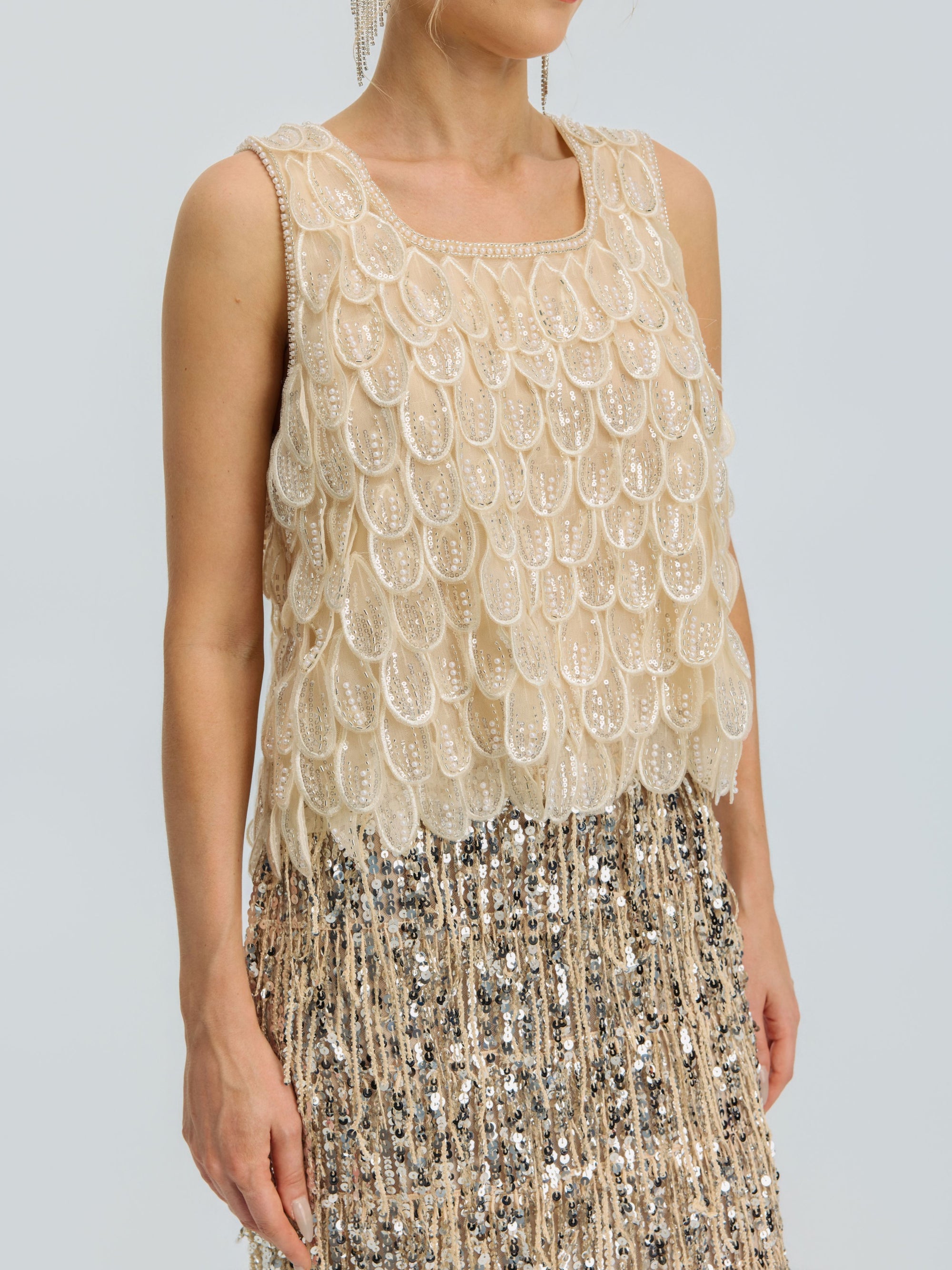 A person wearing the Social Queen 3D Leaf Beaded Mesh Top, a sleeveless style with layered scallop details, paired with a sequined fringe skirt, shown from shoulders to mid-thigh.