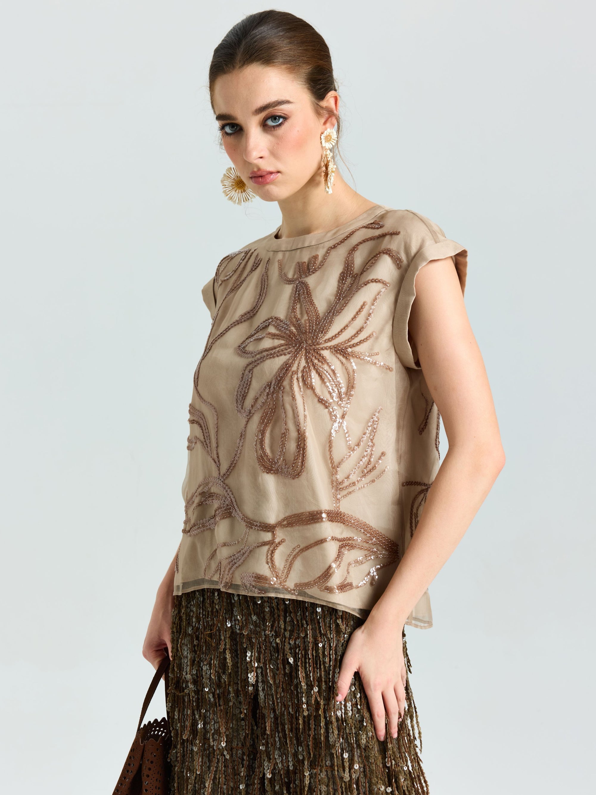 A woman poses against a plain light background in the Social Queen Floral Sequin Embroidered Silk Top and a brown fringed skirt.