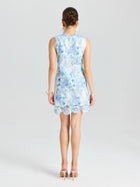 A woman faces away in the Social Queen Embellished Floral Lace Mini Dress, featuring sleeveless light blue lace with organza flowers and paired with beige heels, set against a plain white background.