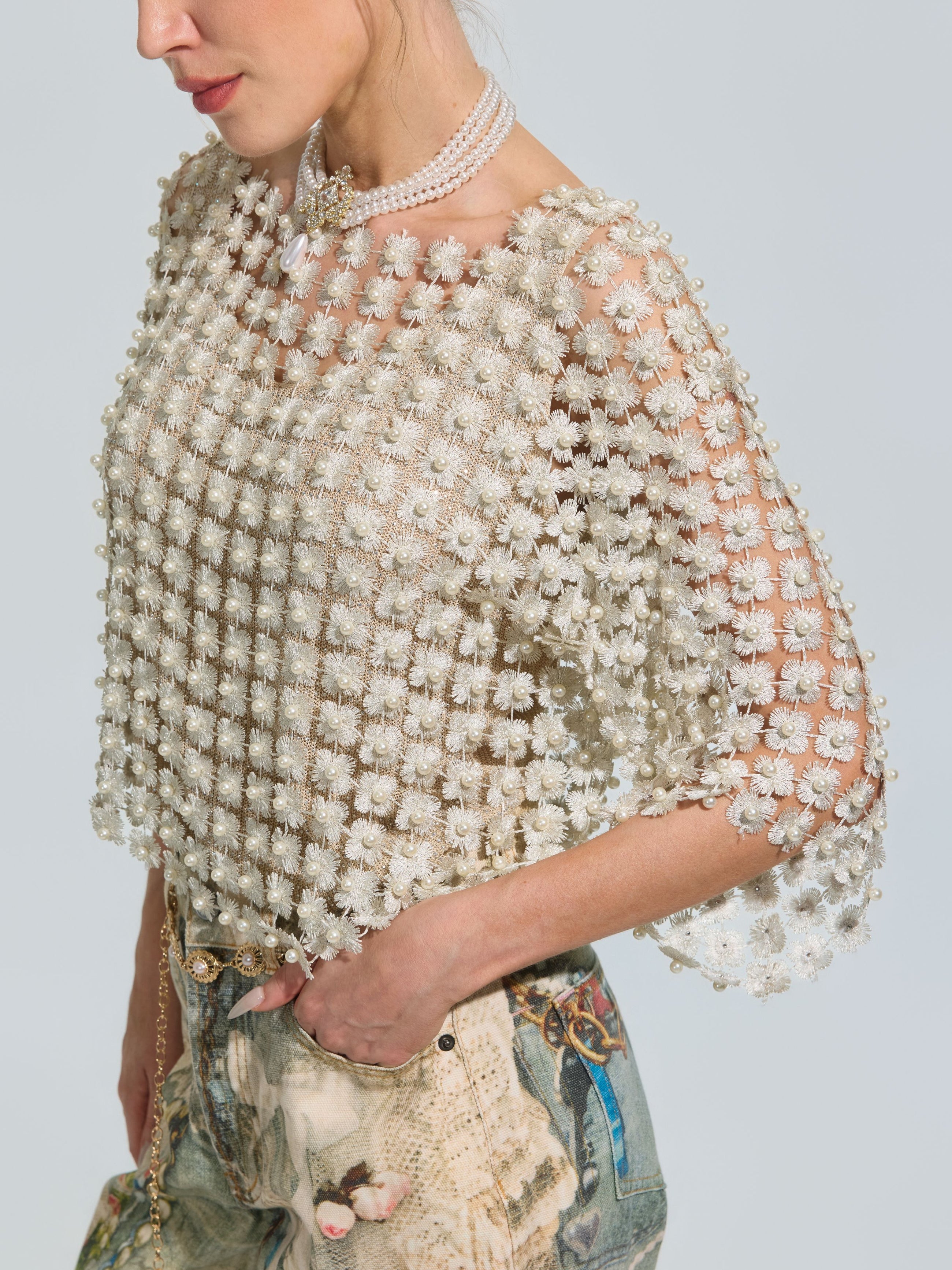 A woman styled in the Social Queen Pearl Daisy Cutwork Top (camisole not included), featuring pearl details and floral patterns, layered over a floral print dress and accessorized with a pearl necklace and chain purse.