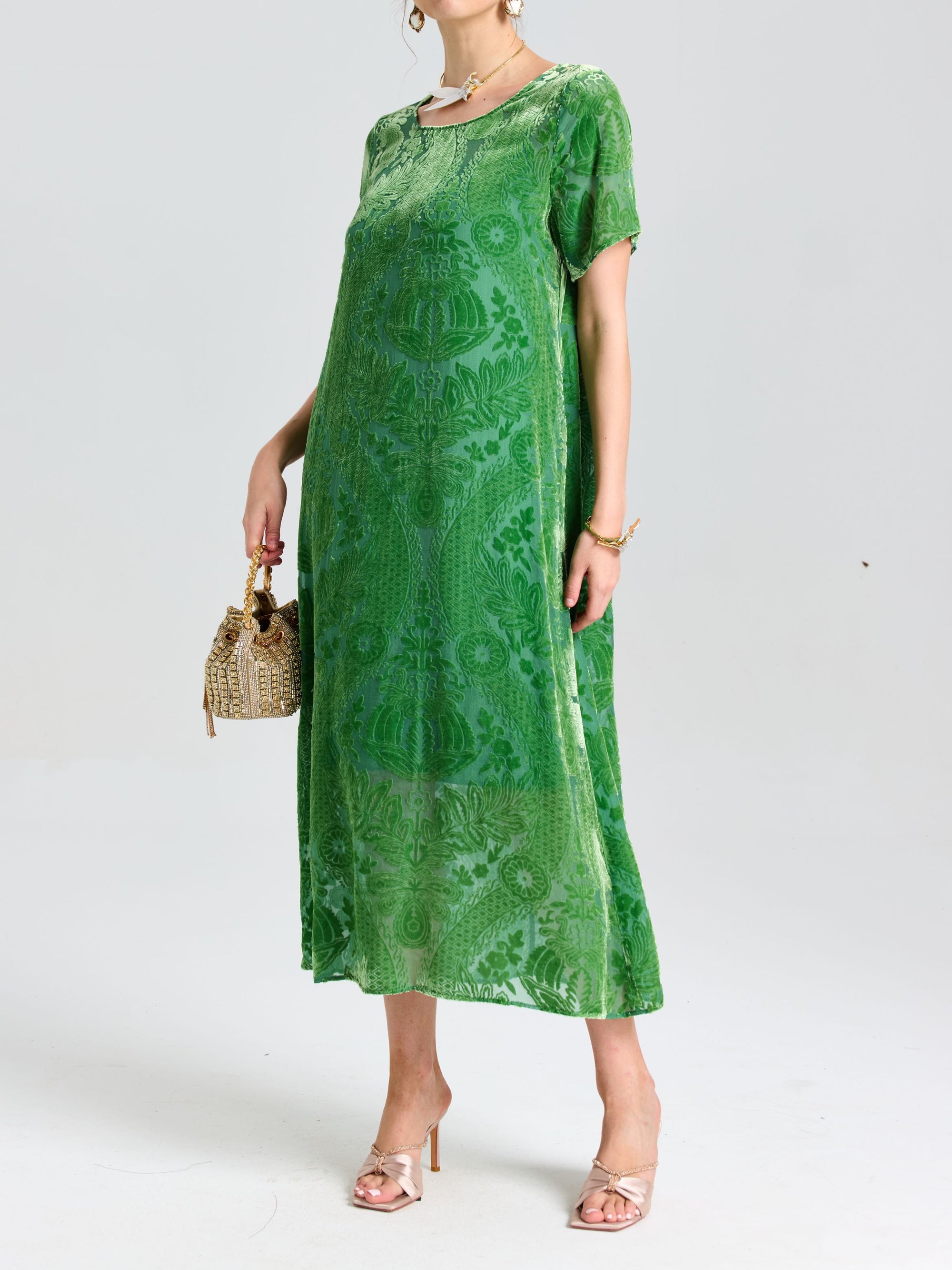 A woman wears the Social Queen Floral Silk Velvet Shift Dress (Cami Included) featuring a green floral pattern and burnout detailing, paired with a woven handbag and nude heels, standing against a plain light background.