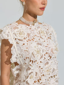 A woman is shown from the shoulders up against a plain background, wearing the Social Queen Pearl Rose Guipure Lace Top—featuring intricate white lace with floral patterns, 3D rose appliqué, and pearl accents—paired with a pearl necklace and pearl earrings.