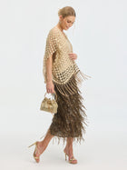 A woman in gold heels and a textured cream top wears Social Queen's Pearl Floral Appliqué Fringe Cape over a bronze fringe skirt, holding a small gold handbag, posing against a plain white background.