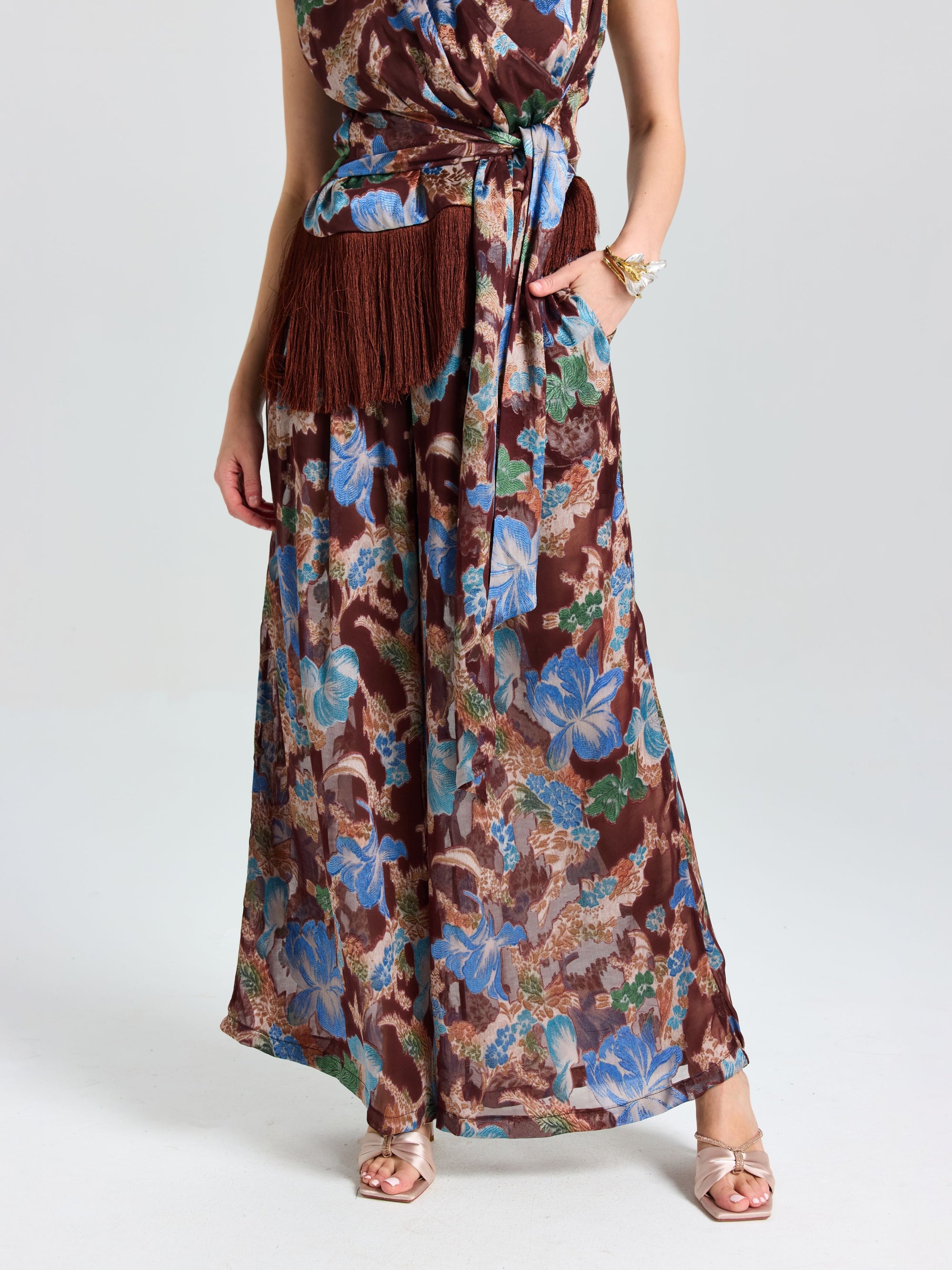 A woman models Social Queen's Floral Print Wide-Leg Pants styled for effortless vacation dressing, pairing gold sandals and standing against a plain background.