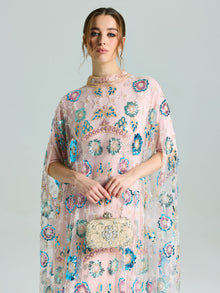 A woman stands against a plain background, wearing the Social Queen Beaded Floral Embellished Cape Gown, and holding a small ornate clutch bag.