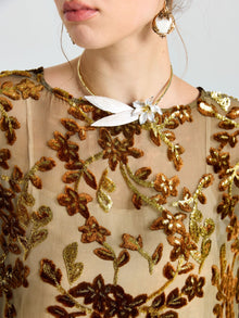 A woman wears the Social Queen Flocked Floral Silk Sheer Top (Camisole Not Included) featuring gold and brown vine-inspired floral embroidery, paired with a gold dragonfly necklace and a statement pearl earring.