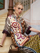 A woman in the Social Queen Patchwork Print Cotton Shirt Dress (belt included) sits on marble stairs, leaning against a wooden banister, with a brown handbag on the step beside her.