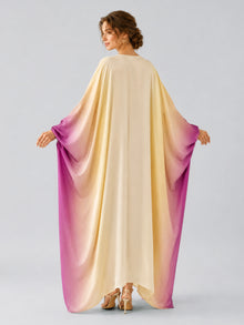 A woman stands with her back to the camera wearing the Social Queen Ombré Beaded Embroidered Cape Dress, which features a satin finish that fades from cream at the top to purple along the sleeves and hem, holding out the fabric to display its elegant drape.