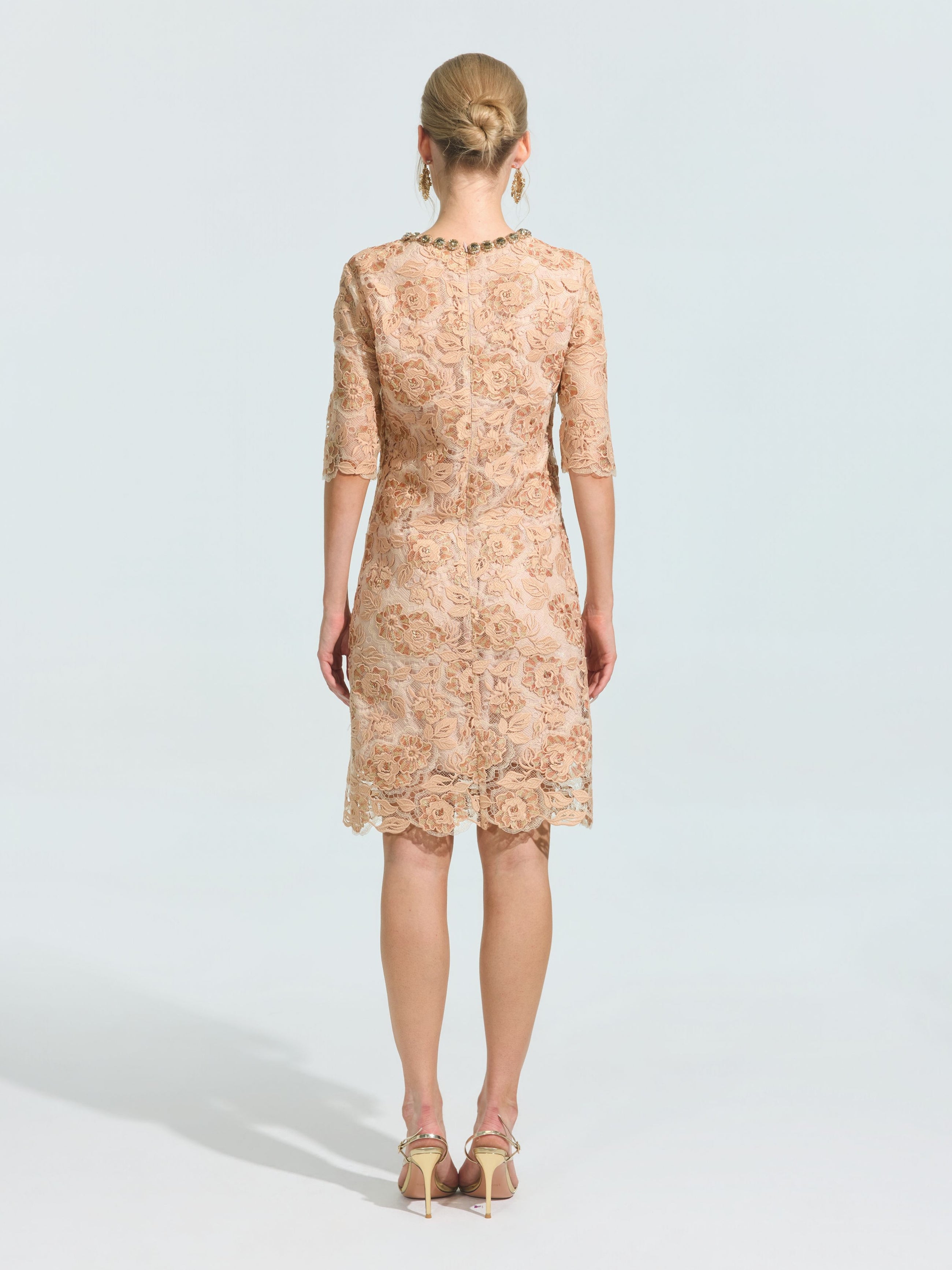 A woman stands with her back to the camera in a Social Queen 3D Floral Appliqué Lace Shift Dress—knee-length, light beige, with delicate floral embroidery and half sleeves—paired with gold heels. Ideal as a special occasion dress.