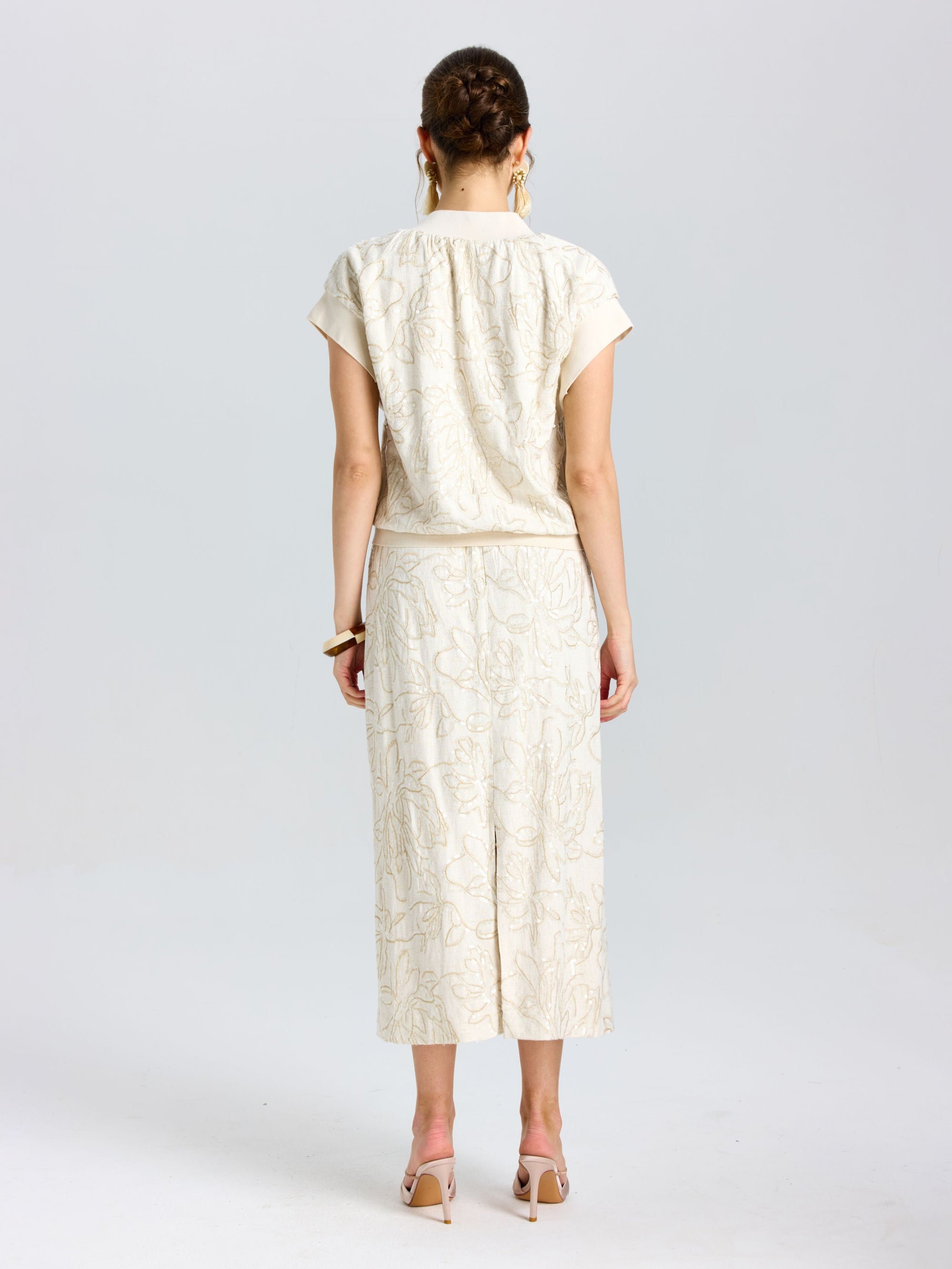 A woman stands with her back to the camera, wearing the Social Queen Floral Embroidered Linen Top, paired with a matching calf-length skirt and high heels.