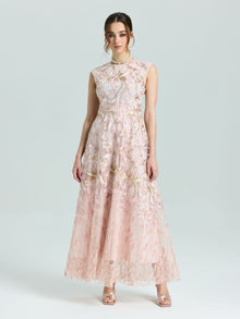 A woman stands against a plain background wearing the Social Queen Gold Floral Embroidered Dress, a sleeveless, floor-length A-line gown, paired with open-toe heels.