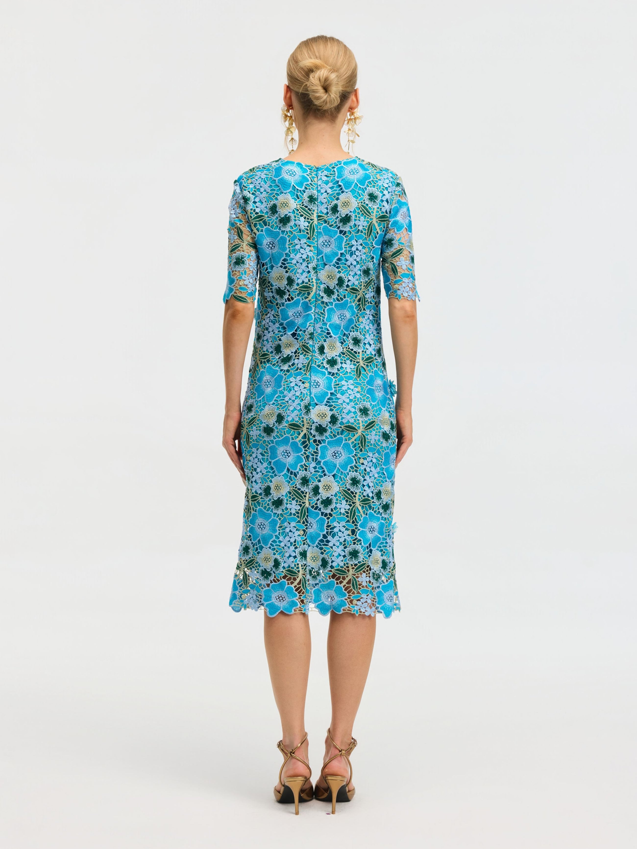 A woman faces away wearing the Social Queen Floral Appliqué Lace Shift Dress with blue water-soluble lace, short sleeves, and knee-length hem, paired with beige high-heeled sandals against a plain white background.