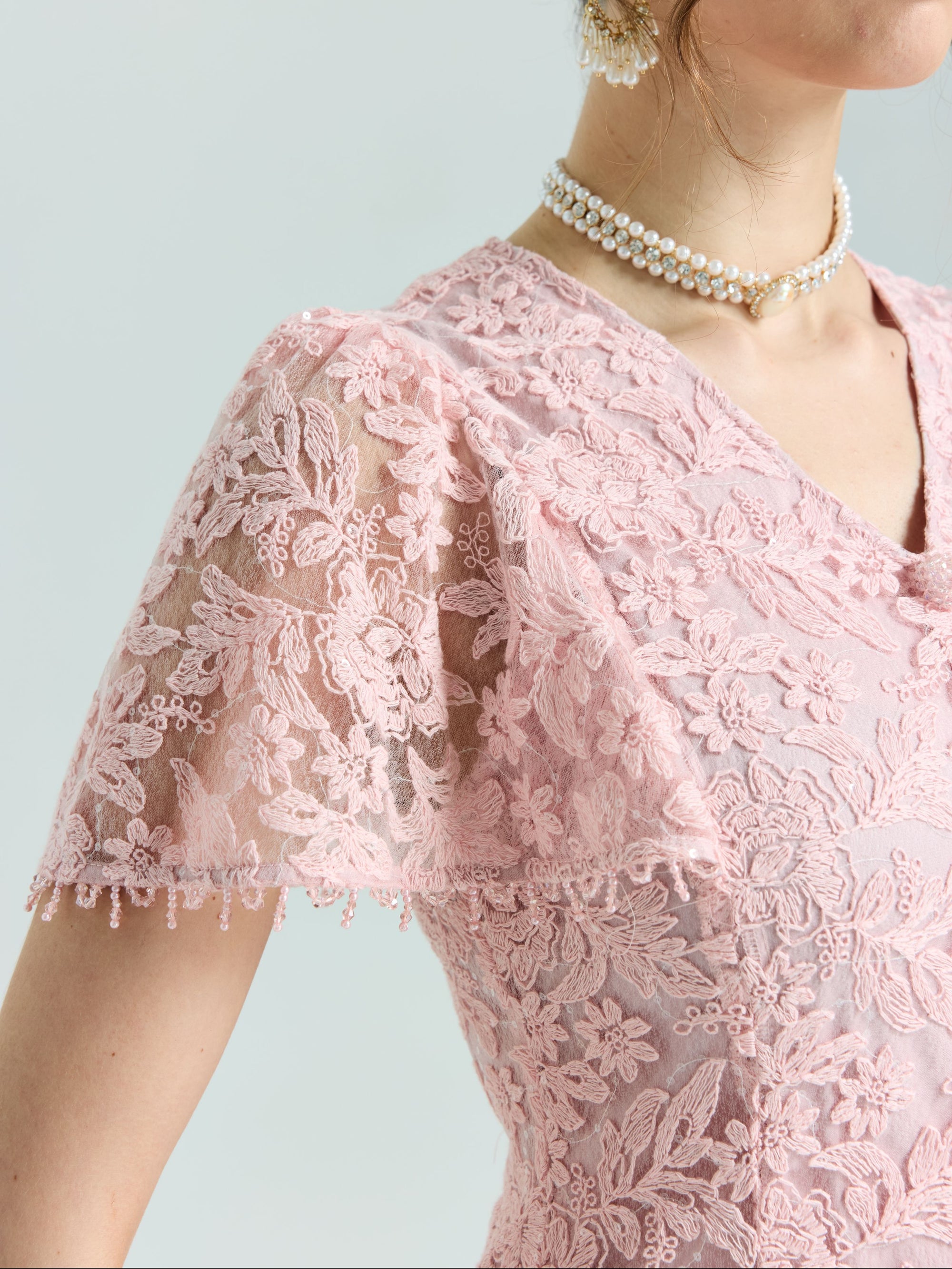 Close-up of a person wearing the Social Queen Floral Embroidered Lace Dress featuring pink lace, short sleeves, beaded details, and a double pearl necklace.