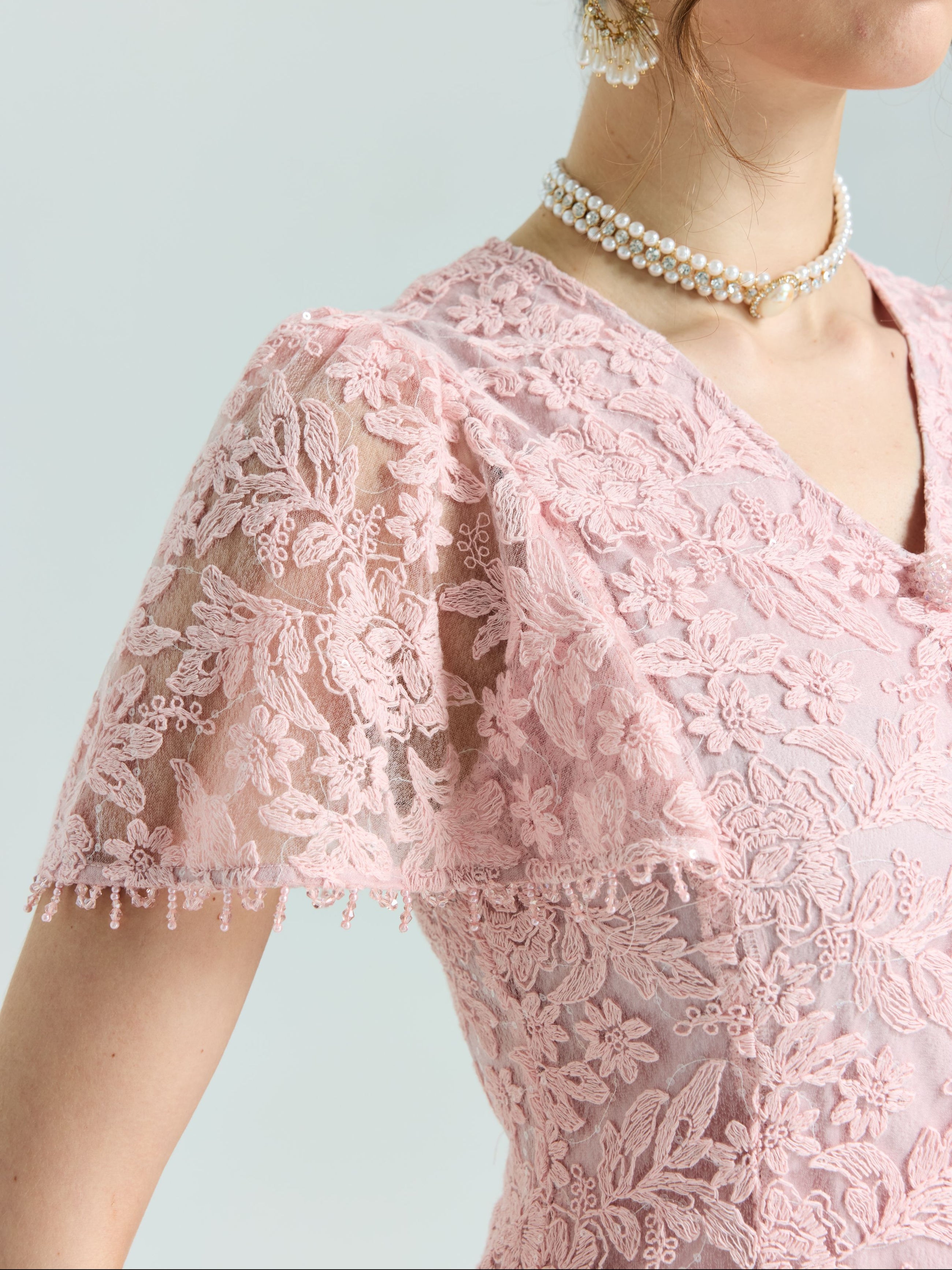 Close-up of a person wearing the Social Queen Floral Embroidered Lace Dress featuring pink lace, short sleeves, beaded details, and a double pearl necklace.