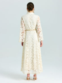 A woman faces away in the Social Queen Embroidered Lace High-Neck Dress, featuring baroque cream floral embroidery with lace-effect, a gold belt, and nude heels, set against a plain light background.