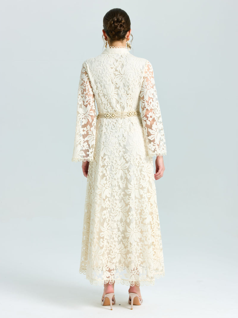 A woman faces away in the Social Queen Embroidered Lace High-Neck Dress, featuring baroque cream floral embroidery with lace-effect, a gold belt, and nude heels, set against a plain light background.