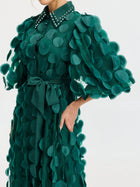 A woman wears the Pearl Embellished Appliqué Dress by Social Queen, featuring textured circular appliqués, puffed sleeves, a belted waist, and a studded collar—a unique twist on the classic polka dot dress.