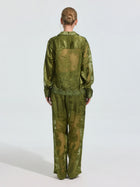 A person stands facing away, wearing Social Queen's Beaded Botanical Burnout Satin Shirt with matching wide-leg pants against a plain light background.