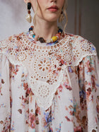 A woman wearing the Social Queen Floral Print Cutwork Linen Dress, featuring a watercolor floral design and a delicate white lace collar, paired with a colorful beaded necklace and a mismatched shell earring. Only the lower half of her face is visible.