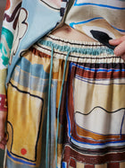 Close-up of a person wearing Social Queen Abstract Print Mulberry Silk Pants, featuring a colorful abstract pattern, elastic waistband, and visible drawstrings. Only the lower torso and hand are visible.
