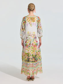 A person stands facing away in the Social Queen Garden Print Silk Dress (Slip Dress Included), featuring a long white silk design with colorful watercolor garden print and gold sandals against a plain background.