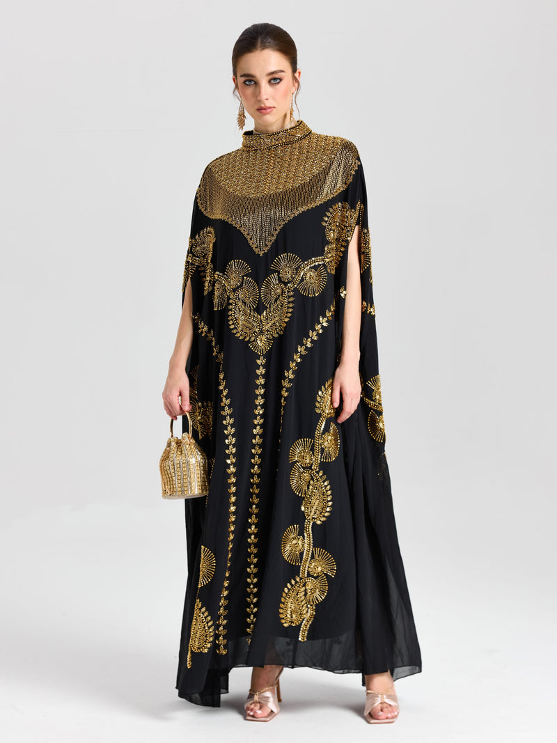 A woman in the Social Queen Beaded Embroidered Cape Dress with Persian-inspired details, holding a small gold handbag and standing against a light background—an elegant choice for evening events.