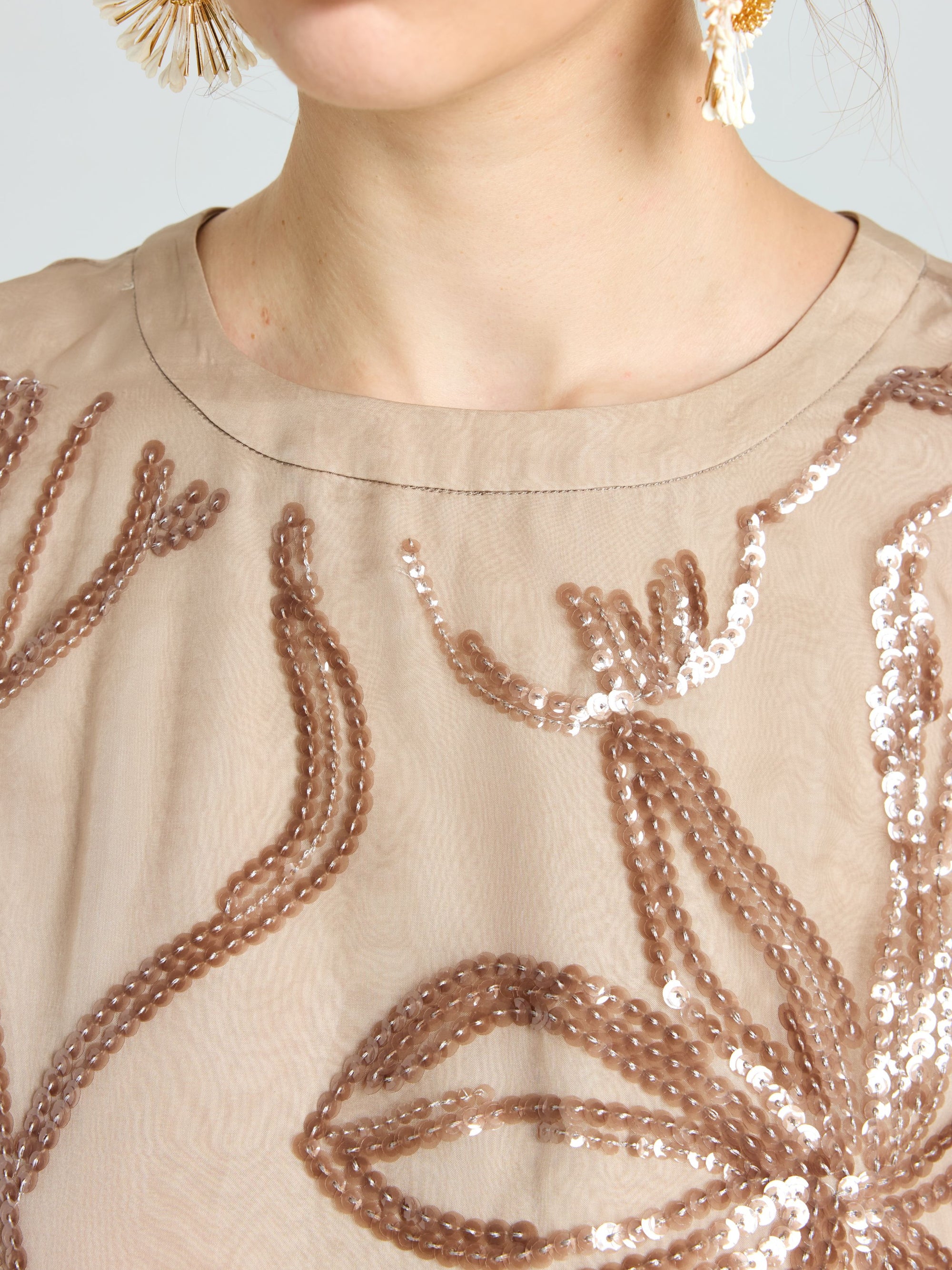 Close-up of a woman wearing the Social Queen Floral Sequin Embroidered Silk Top in beige, paired with large dangling earrings.