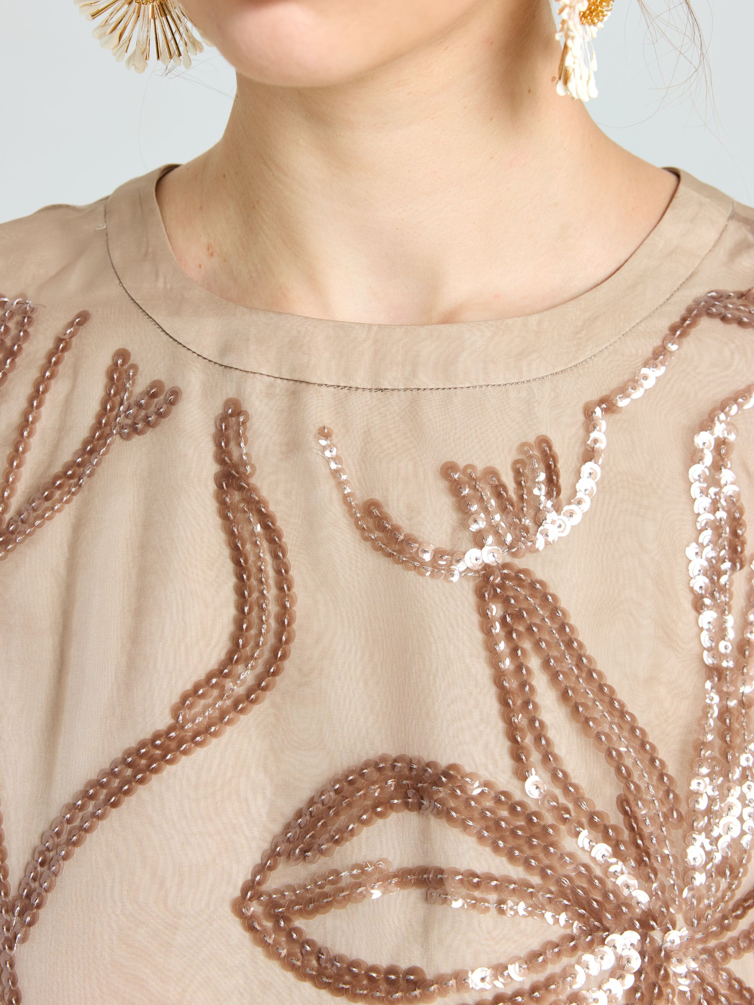 Close-up of a woman wearing the Social Queen Floral Sequin Embroidered Silk Top in beige, paired with large dangling earrings.