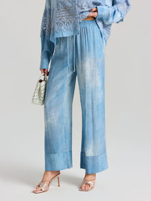A person in Social Queen’s Washed Silk Wide-Leg Pants in light blue, paired with a matching lacy top, heeled sandals, and a small white handbag.