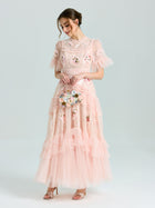A woman in the Social Queen Embroidered Ruffle Tiered Tulle Dress, light pink with floral and sequin embroidery, holds a small bouquet while standing against a plain light background.