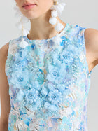A woman in the Social Queen Embellished Floral Lace Mini Dress, featuring sleeveless pastel lace with large blue organza flowers, paired with white flower earrings.