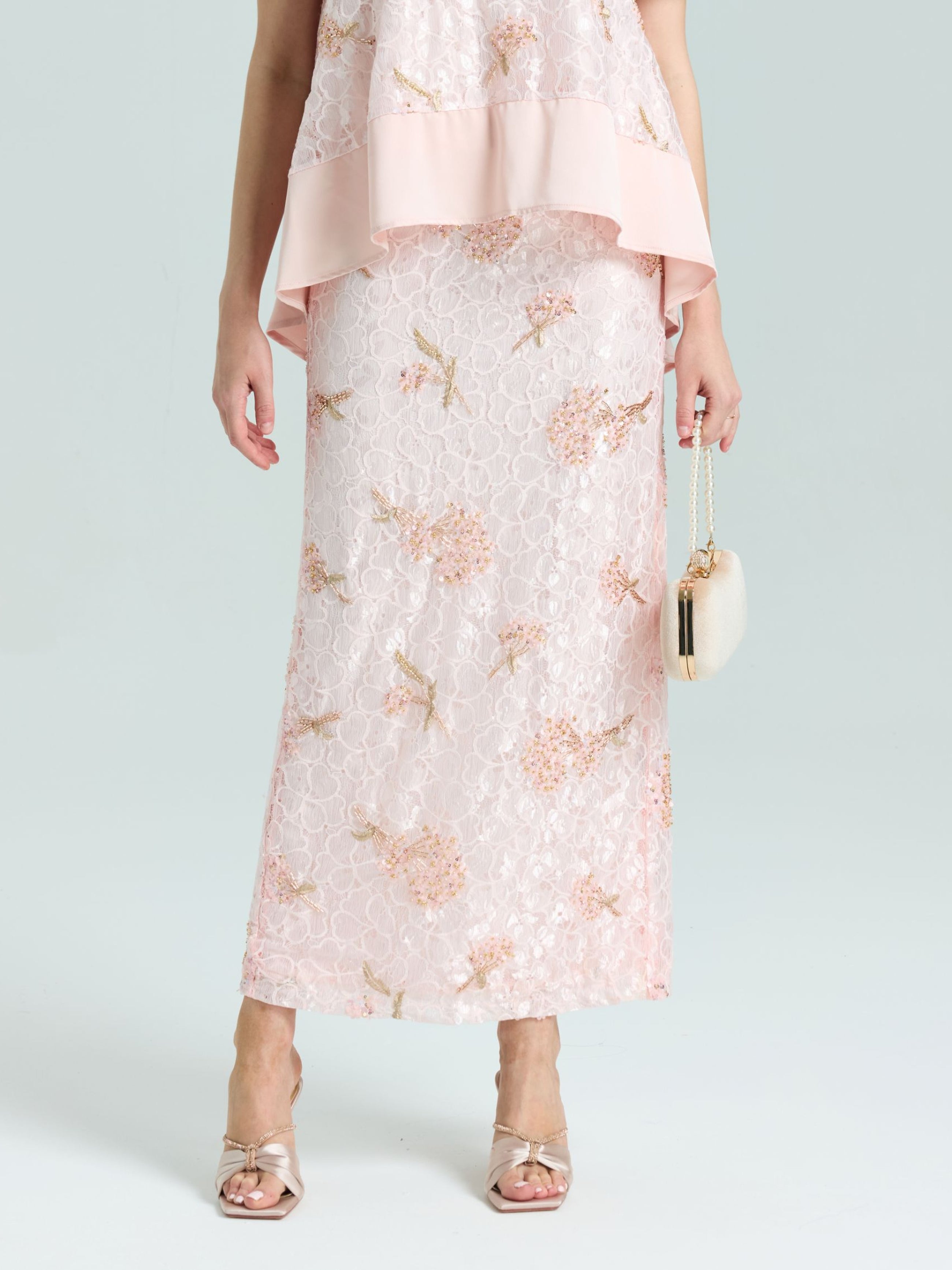 A person wears the Social Queen Dragonfly Beaded Lace Midi Skirt in pale pink with a matching top and holds a small white purse, showing only the lower half of their straight silhouette.
