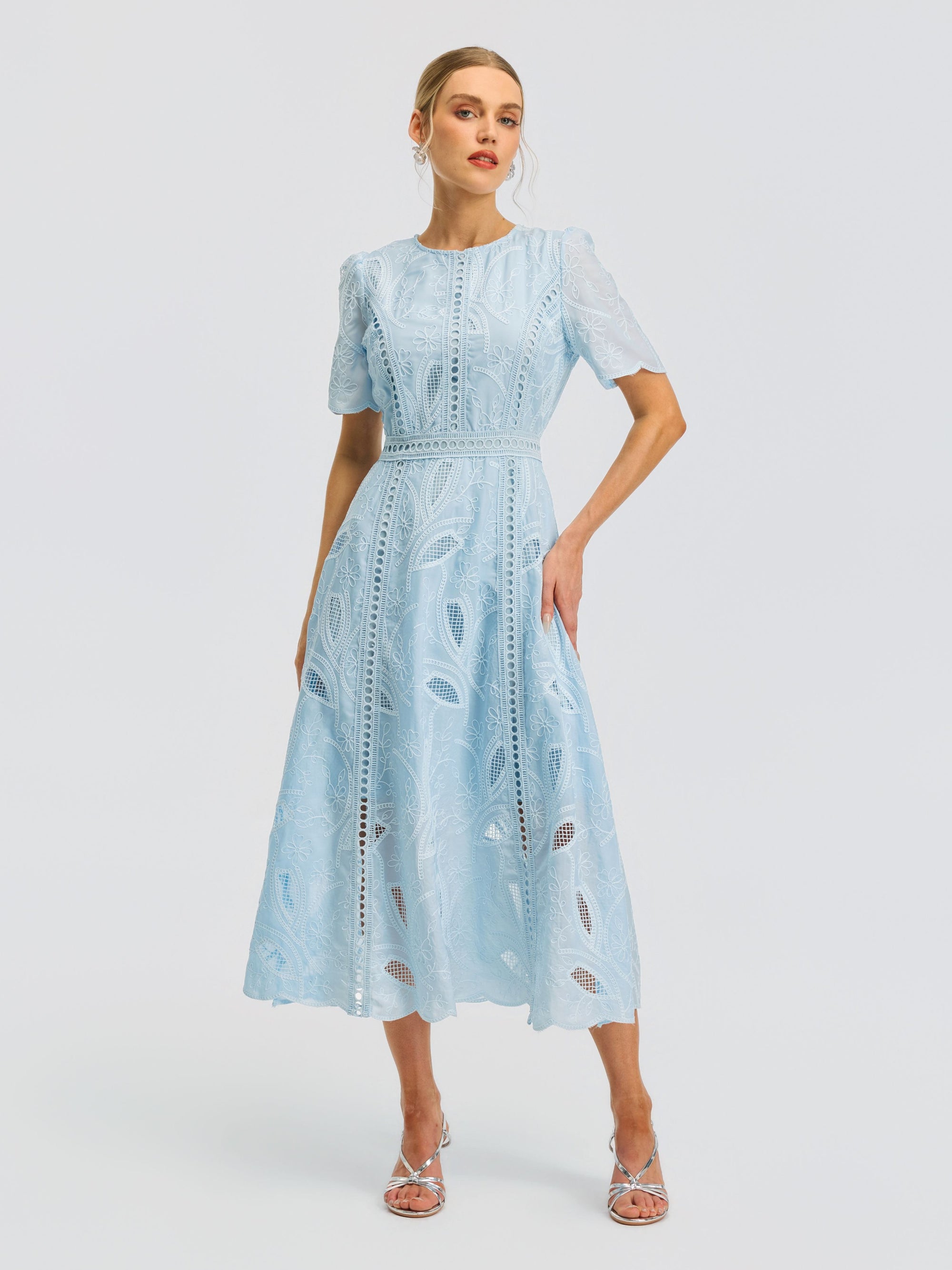 A woman wearing the Social Queen Floral Cutwork Embroidered Dress—a light blue, lace midi dress with short sleeves, intricate leaf patterns, and delicate floral embroidery—stands against a plain white background.