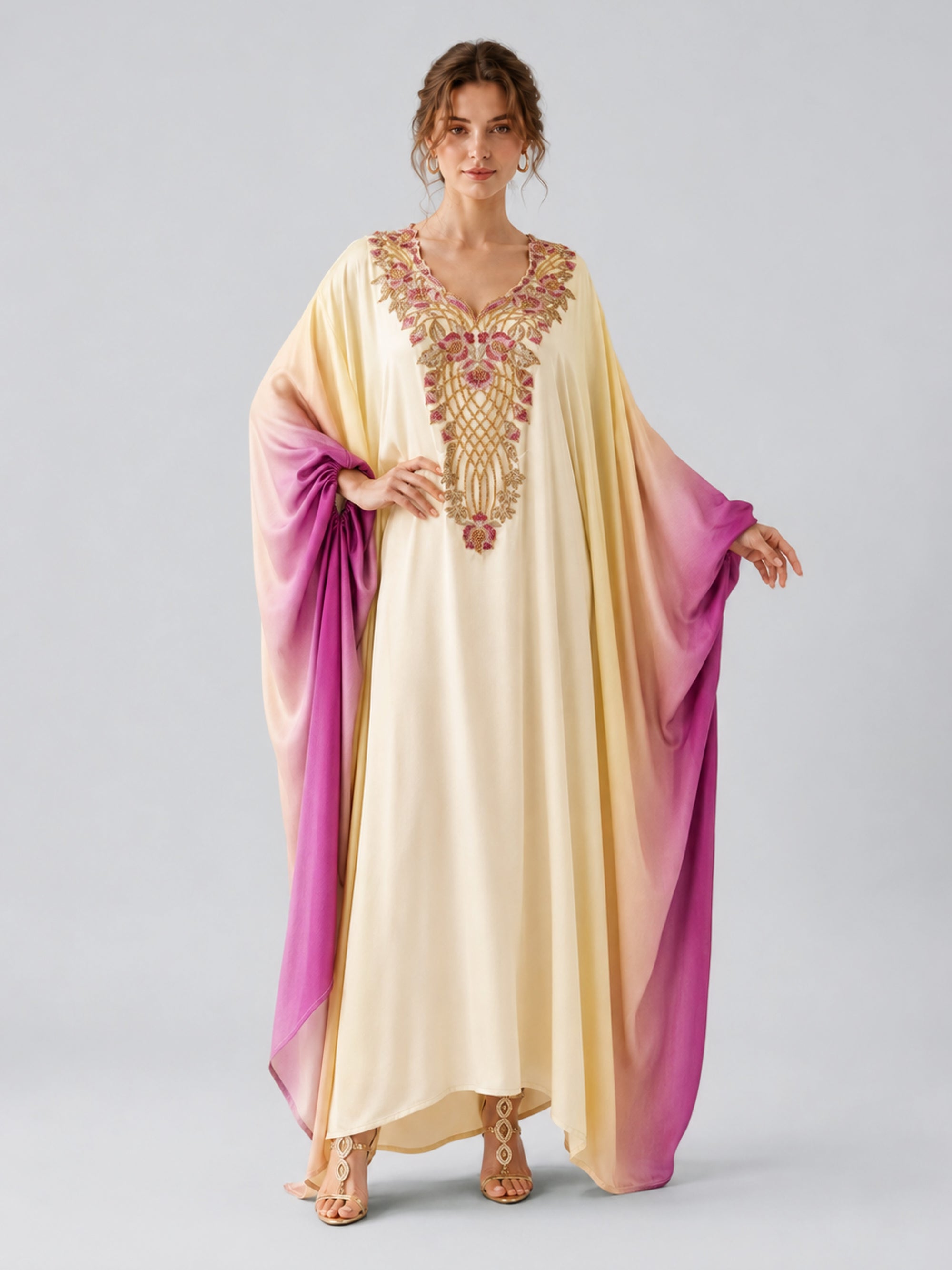 A person stands facing forward against a plain background, wearing the Social Queen Ombré Beaded Embroidered Cape Dress—its flowing cream and purple hues adorned with ornate gold and pink embroidery that echoes the elegance of a cape silhouette maxi.