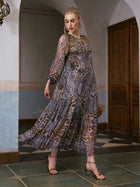 A woman stands indoors wearing the Social Queen Leopard Paisley Print Silk Dress, paired with gold high heels and a brown clutch. Posing with one foot forward, she looks down.