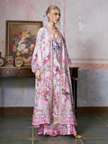 A woman stands indoors near a table with framed photos and a flower painting on the wall behind her, elegantly wearing the Social Queen Baroque Print Mulberry Silk Robe with Scarf, an ensemble evocative of luxury resort wear.